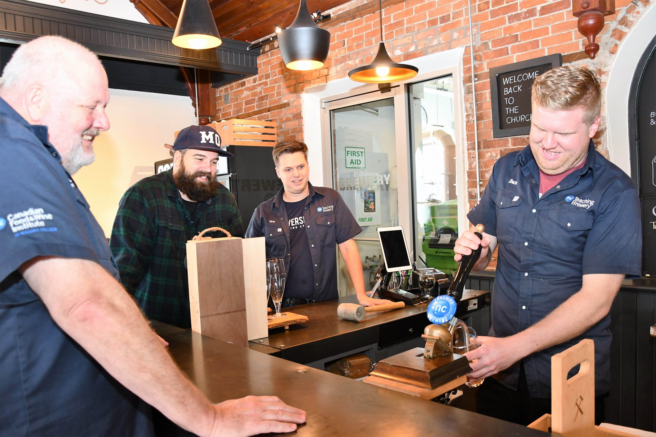 NC Brewmaster student Dan Clark pours a pint of his beer, Loggerhead, from behind the bar at Silversmith as Jon Downing (NC Brewmaster professor), Ben Goerzen (Silversmith marketing and communications), and Ian Evans (NC Brewmaster student) look on.