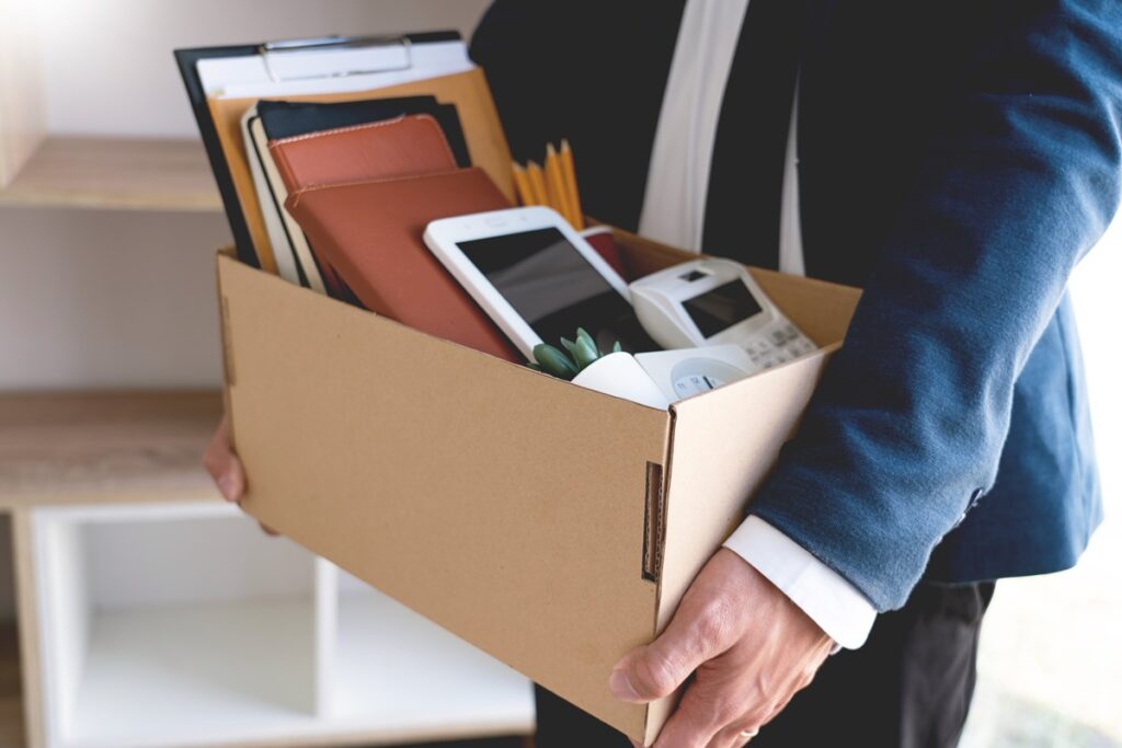 A man wearing a suit holds a cardboard box containing the personal items from an office desk