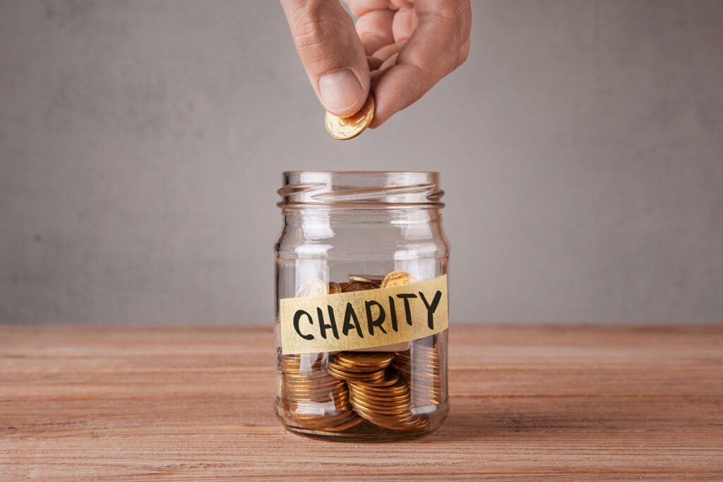 A hand drops a coin into a glass jar labelled "charity"