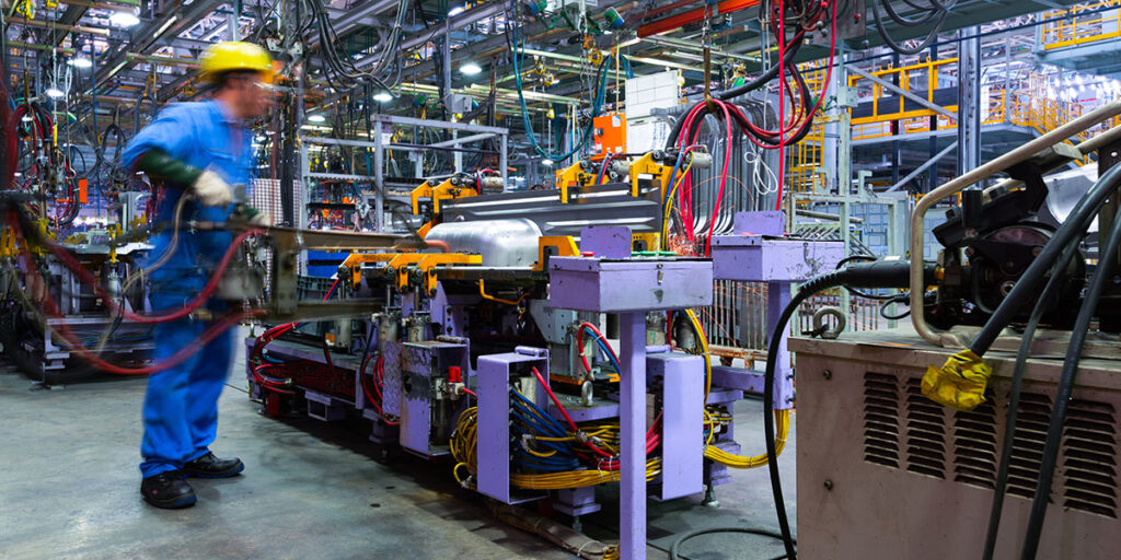 A worker in blue overalls and a hard hat operates a machine in a factory