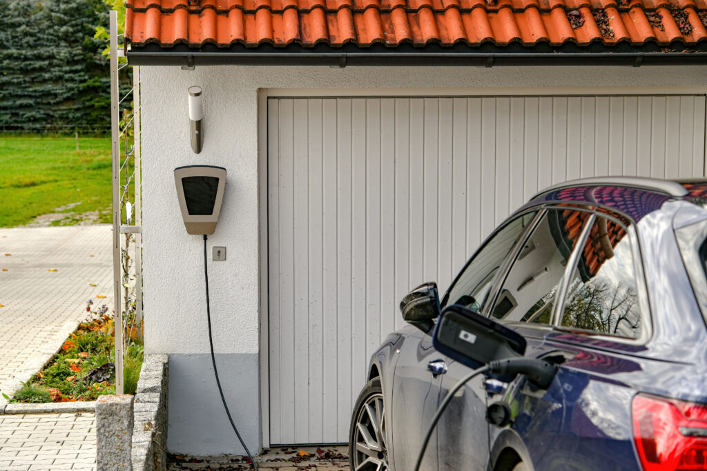 An electric car being charged in front of a garage