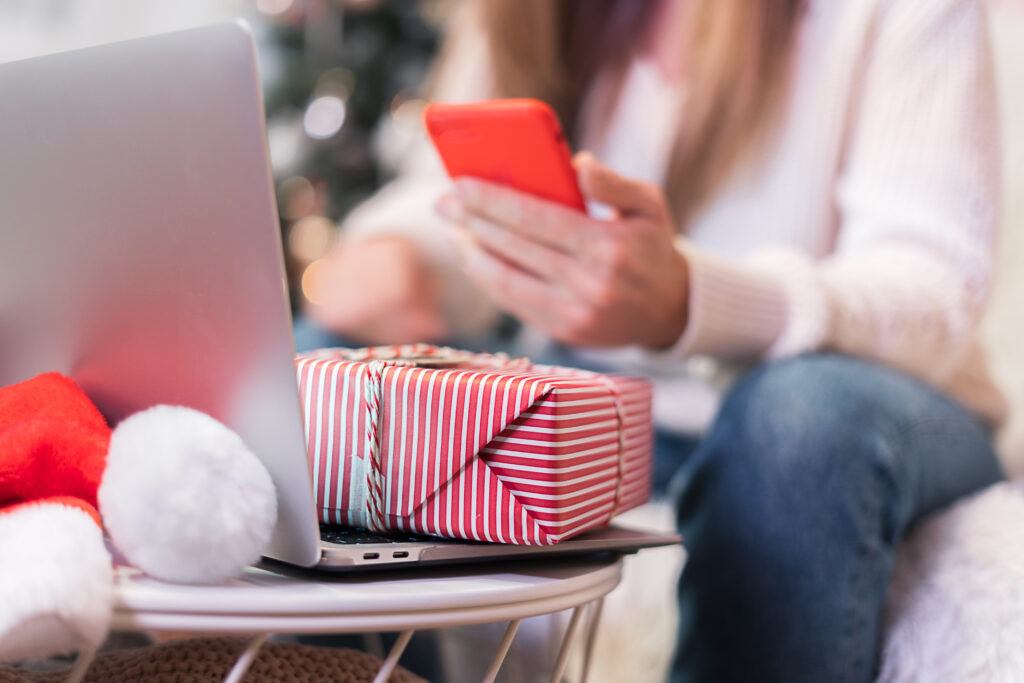 A woman shopping online with a mobile phone and a laptop with a gift 