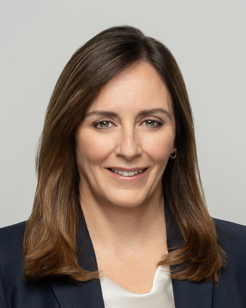 Incoming OPG CEO Nicolle Butcher. A headshot of a white woman with long brown hair wearing dark business dress.