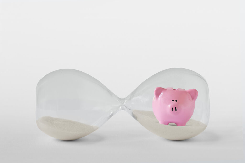 An hourglass on its side with a pink piggy bank in one bulb