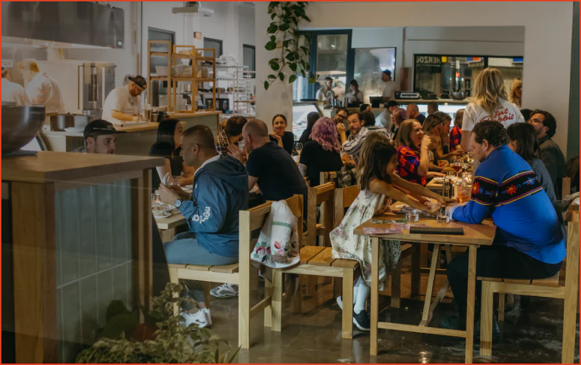 The crowded interior of the Fat Rabbit butcher shop. People and families sit at wooden tables to dine.