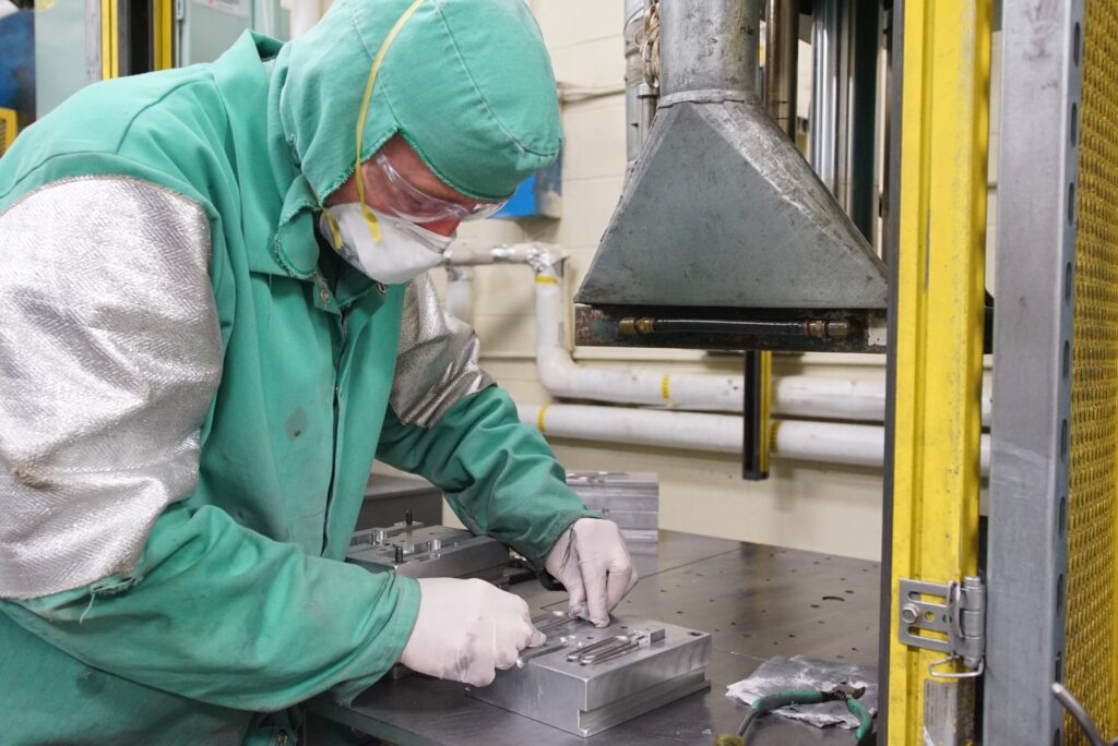 A metalworker wearing full protective gear works on a metal casting in a factory