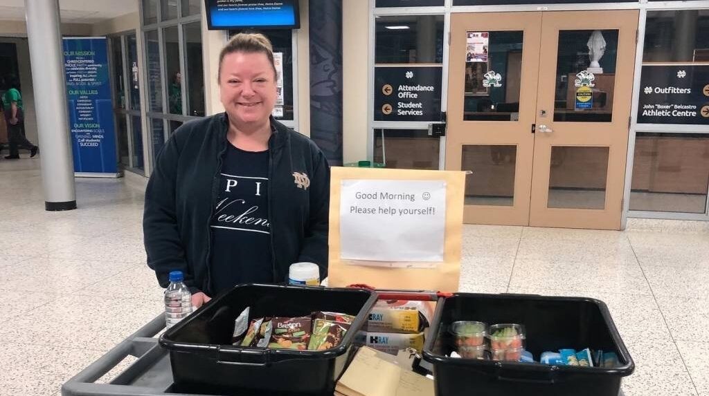 A woman stands behind a cart laden with free foodstuffs in a school