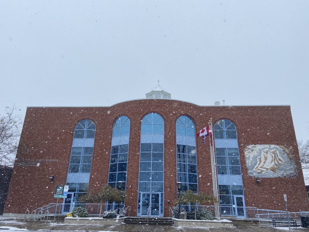 An exterior view of Port Colborne City Hall, a large red brick building with large blue windows in the front, during snowfall.