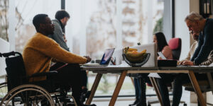 Inclusive work culture depicted with multi-ethnic team including a person with a disability engaging in a collaborative work session in a bright office.