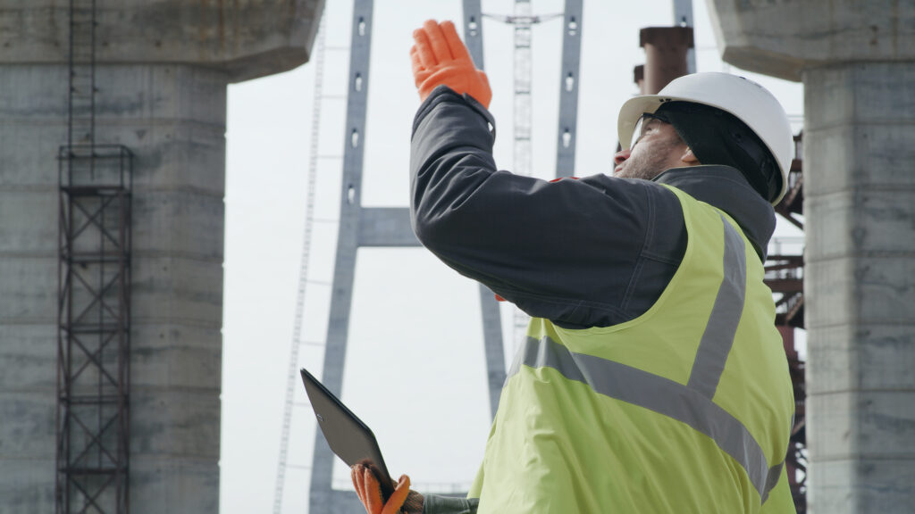 An engineer wearing a hard hat and a hi-viz vest directs the construction of a bridge